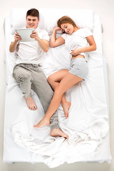 The young lovely couple lying in a bed with laptop — Stock Photo, Image
