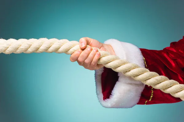 Ręka Świętego Mikołaja, ciągnięcie liny na niebieskim tle — Zdjęcie stockowe