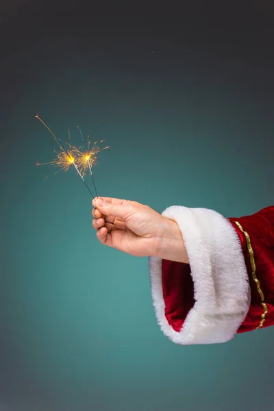 Mano de Santa Claus sosteniendo un bengalas sobre fondo azul —  Fotos de Stock