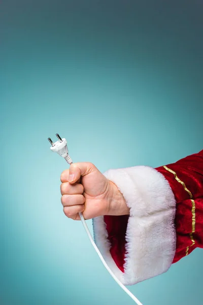 Mano de Santa Claus sosteniendo un enchufe eléctrico sobre fondo azul — Foto de Stock