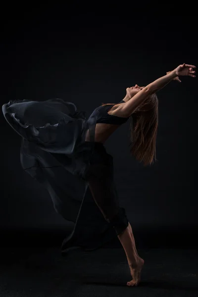 Молодая красивая танцовщица в бежевом платье танцует на черном фоне — стоковое фото