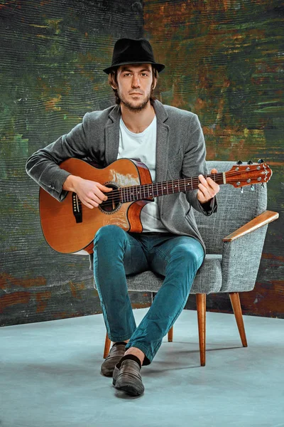 Tipo fresco con sombrero tocando la guitarra sobre fondo gris — Foto de Stock