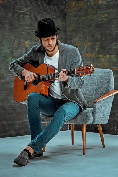 Tipo fresco con sombrero tocando la guitarra sobre fondo gris — Foto de Stock