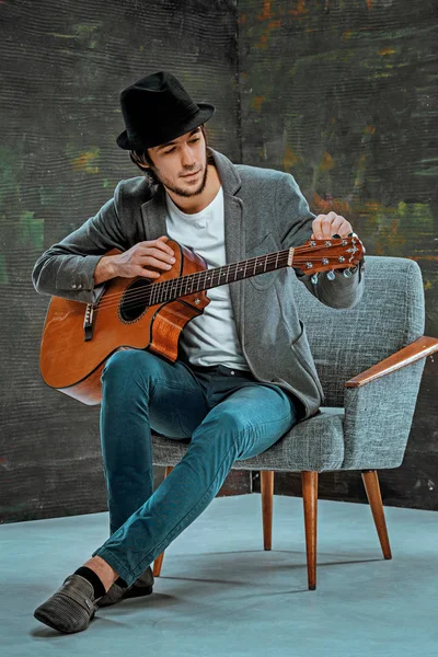 Крутой парень в шляпе играет на гитаре на сером фоне — стоковое фото