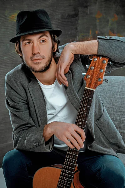 Cool guy sitting with guitar on gray background — Stock Photo, Image