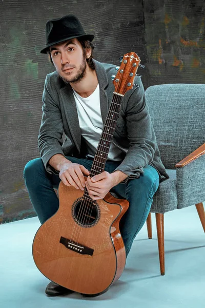 Cool guy sitting with guitar on gray background — Stock Photo, Image