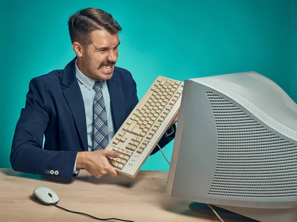 Empresario enojado rompiendo teclado contra fondo azul —  Fotos de Stock