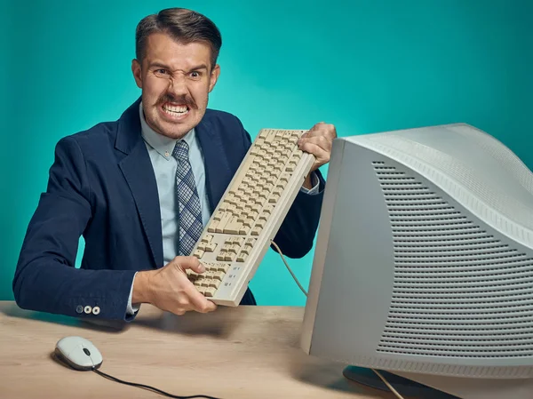 Empresario enojado rompiendo teclado contra fondo azul — Foto de Stock