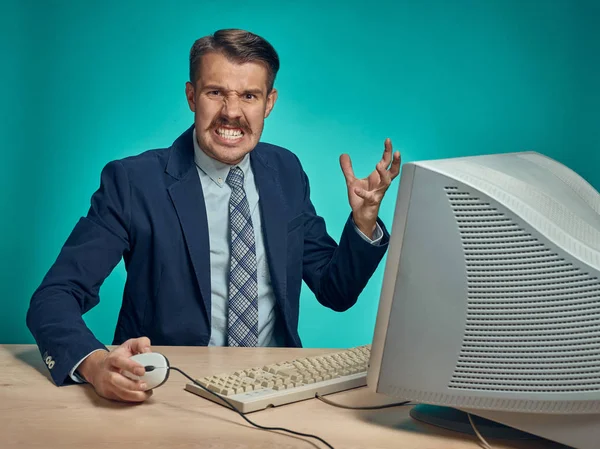 Hombre de negocios enojado usando un monitor contra fondo azul — Foto de Stock