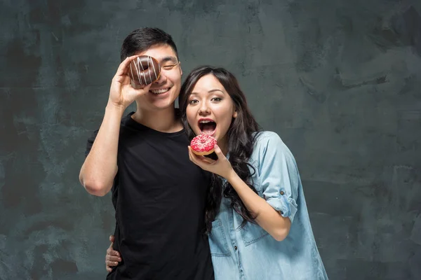 Молода азіатська пара насолоджується їжею солодкого барвистого пончика — стокове фото