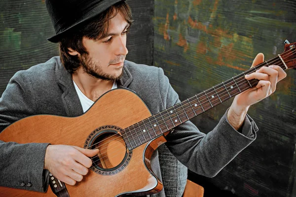 Tipo fresco con sombrero tocando la guitarra sobre fondo gris — Foto de Stock