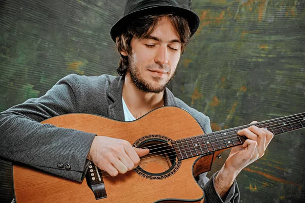 Tipo fresco con sombrero tocando la guitarra sobre fondo gris — Foto de Stock