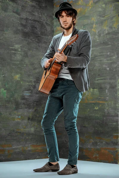 Tipo fresco con sombrero tocando la guitarra sobre fondo gris — Foto de Stock