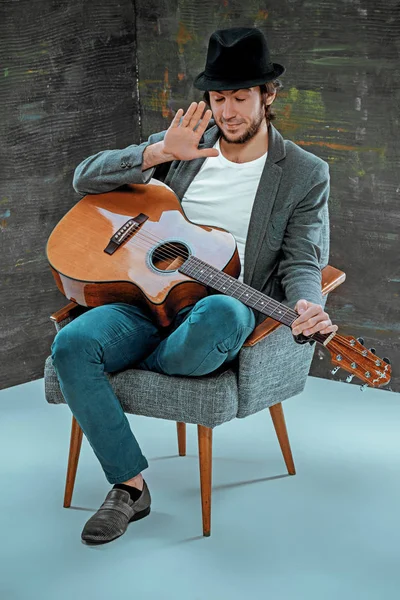 Cool guy sitting with guitar on gray background — Stock Photo, Image