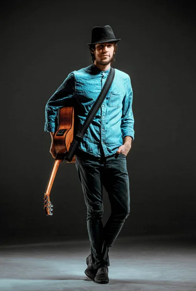 Cool guy standing with guitar on dark background — Stock Photo, Image