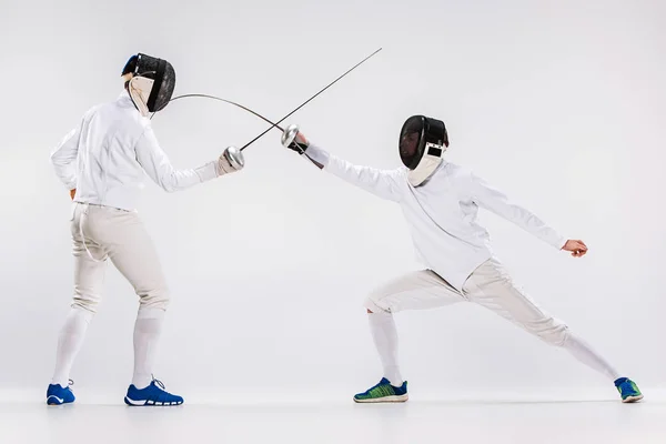 Los dos hombres con traje de esgrima practicando con espada contra gris — Foto de Stock