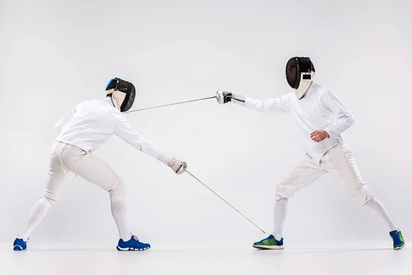 I due uomini indossano una tuta da scherma che si esercitano con la spada contro il grigio — Foto Stock