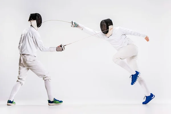The two men wearing fencing suit practicing with sword against gray