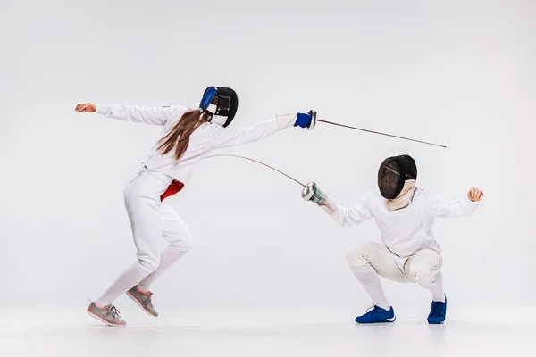 Los hombres y mujeres que usan traje de esgrima practicando con espada contra gris — Foto de Stock