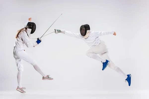 Les hommes et les femmes portant un costume d'escrime pratiquant l'épée contre le gris — Photo