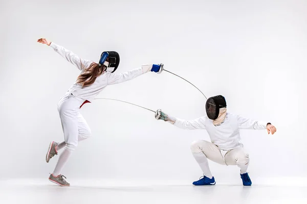 La donna e l'uomo che indossano una tuta da scherma che si esercitano con la spada contro il grigio — Foto Stock