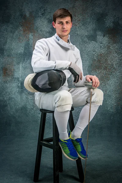 The man wearing fencing suit with sword against gray