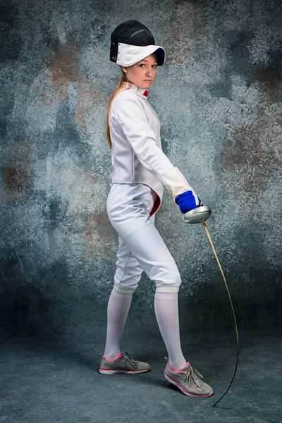 The woman wearing fencing suit with sword against gray