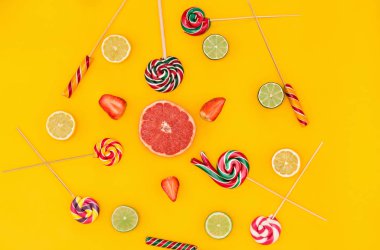 Taze narenciye meyve ile turuncu arka plan üzerinde renkli şekerler