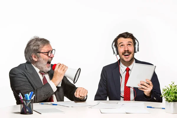 The two colleagues working together at office on white studio background. one man shouting through a megaphone - other in headphones can not hear nothing