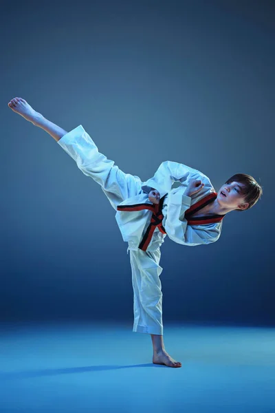 Jonge jongen opleiding karate op blauwe achtergrond — Stockfoto