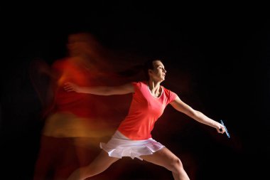 Genç kadın siyah arka plan üzerinde badminton oynarken