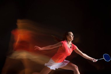 Genç kadın siyah arka plan üzerinde badminton oynarken