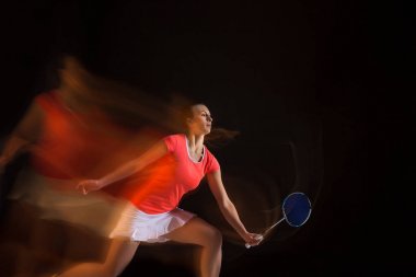 Genç kadın siyah arka plan üzerinde badminton oynarken