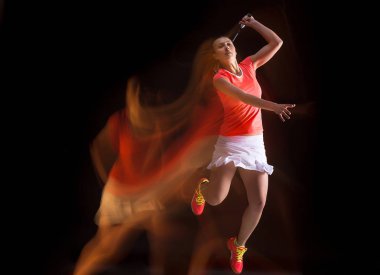 Genç kadın siyah arka plan üzerinde badminton oynarken