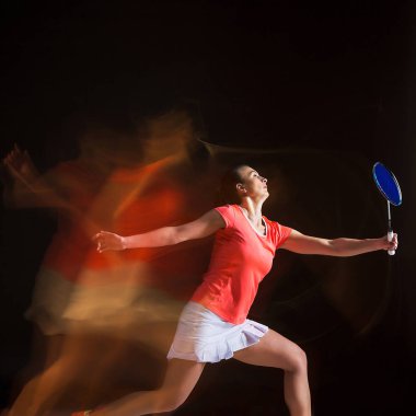 Genç kadın siyah arka plan üzerinde badminton oynarken