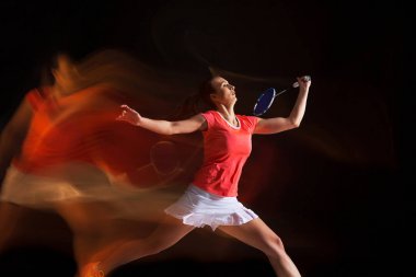 Genç kadın siyah arka plan üzerinde badminton oynarken