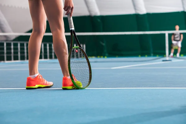 Benen van jong meisje in een gesloten tennisbaan en racket en bal — Stockfoto