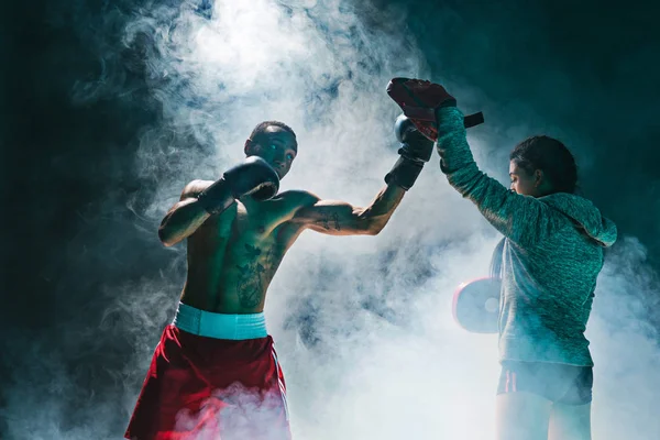 Красавчик афро-американский боксер с голым туловищем практикует удары с партнером в бойцовском клубе — стоковое фото