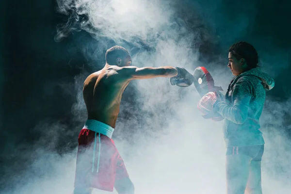 Bonito boxeador afro-americano com tronco nu está praticando socos com um parceiro no clube de luta — Fotografia de Stock