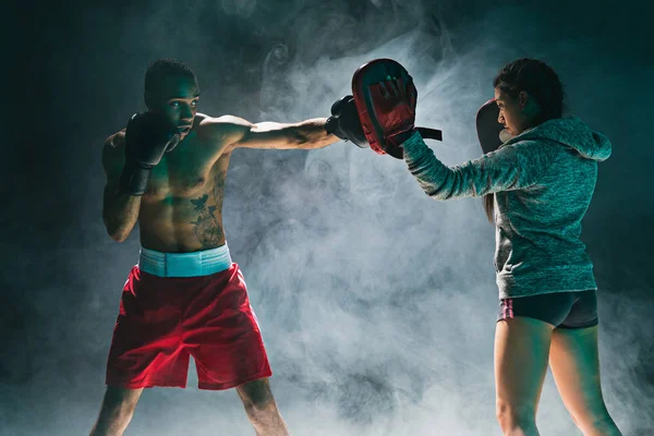 Guapo boxeador afroamericano con torso desnudo está practicando golpes con un compañero en el club de lucha — Foto de Stock