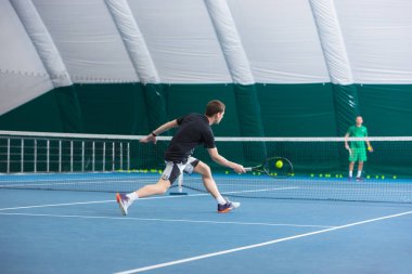 Genç adam bir kapalı Tenis Kortu top ve raket ile yerleştirmek