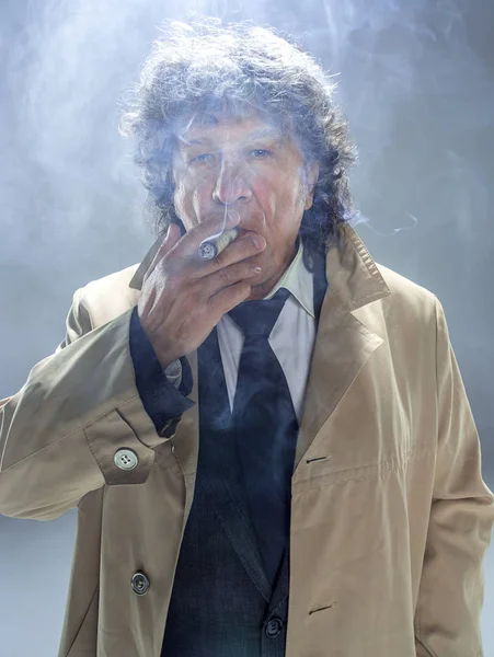 Старший человек с сигарой в качестве детектива или босса мафии на сером фоне студии — стоковое фото