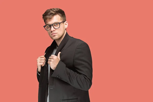 Junger gutaussehender Mann in schwarzem Anzug und Brille isoliert auf rotem Hintergrund — Stockfoto