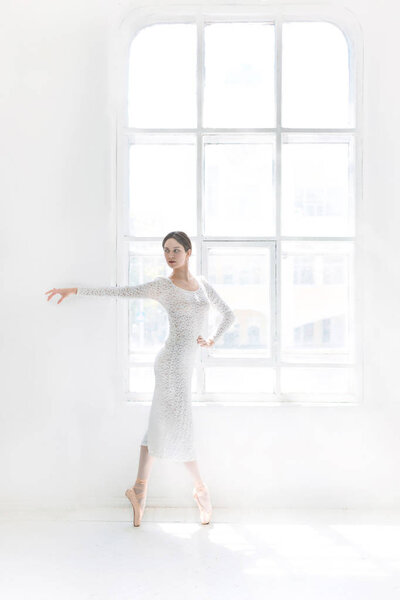 Young and incredibly beautiful ballerina is posing and dancing in a white studio