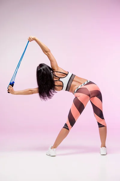 The woman training against pink studio with jump rope