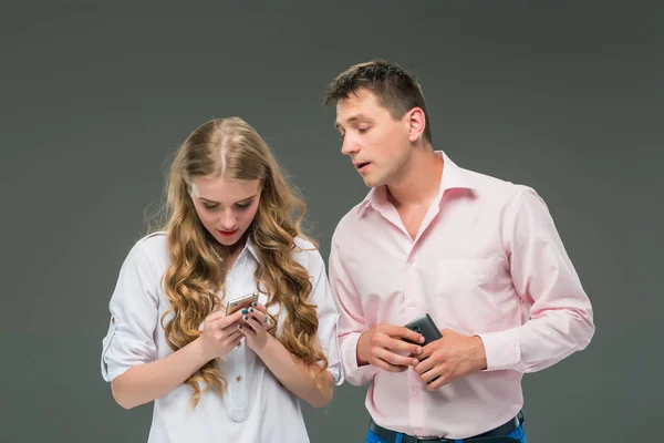 Concepto de negocio. Los dos jóvenes colegas sosteniendo teléfonos móviles sobre fondo gris —  Fotos de Stock