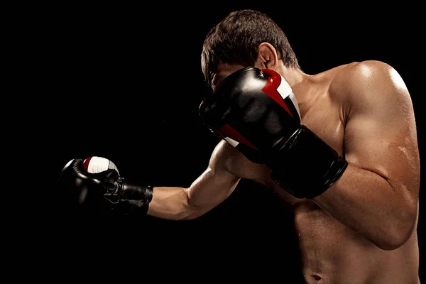 Male boxer boxing in punching bag with dramatic edgy lighting in a dark studio — Stock Photo, Image