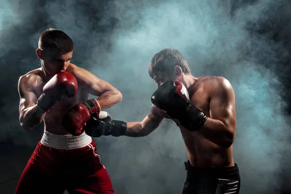 Two professional boxer boxing on black smoky background, — Stock Photo, Image