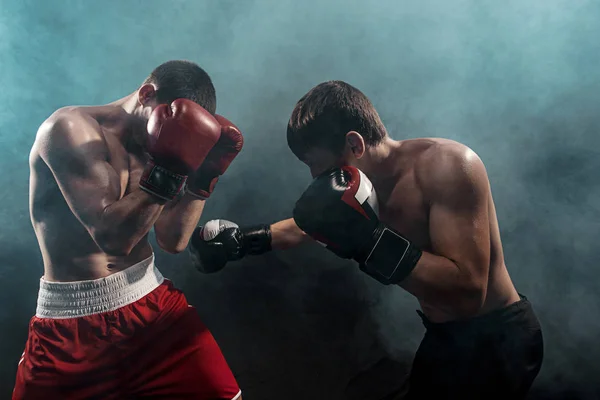 Two professional boxer boxing on black smoky background, — Stock Photo, Image