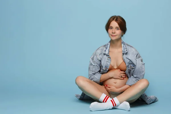 青色の背景の上に座って若い美しい妊娠中の女性 — ストック写真